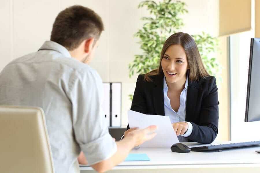 Woman in business suit smiling at man with paperwork in her hand