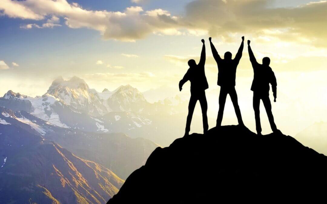 three people unite at top of a mountain