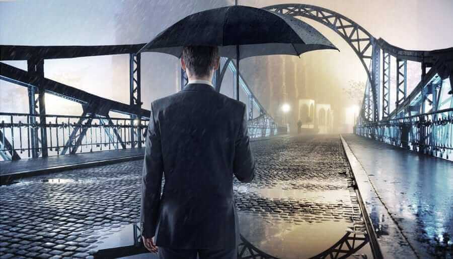 Business Man holding Umbrella in the rain looking towards a brighter future