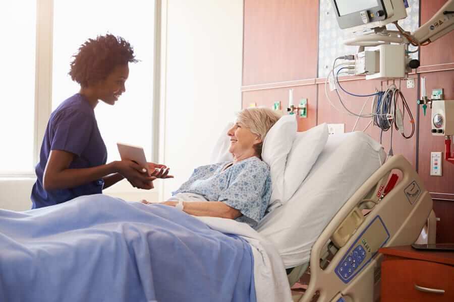 Nurse and elderly woman in hospital bed smiling