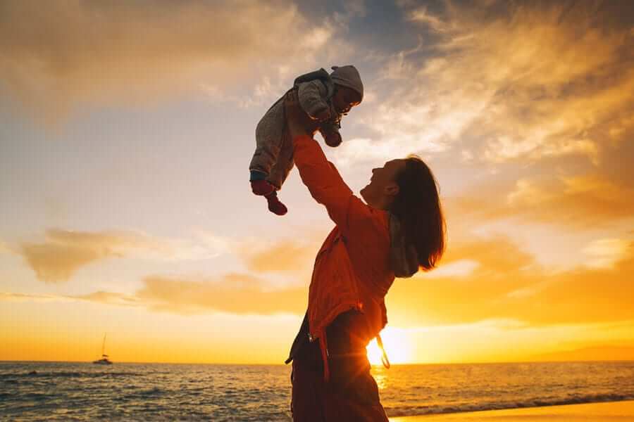Mother holding baby over beach sunset
