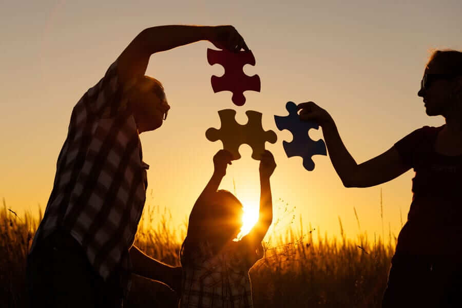 Family holding puzzle pieces in front of sunset