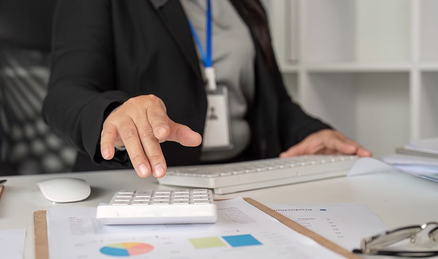 Middle-aged business woman in a modern office, working on paperwork with financial documents and a calculator.